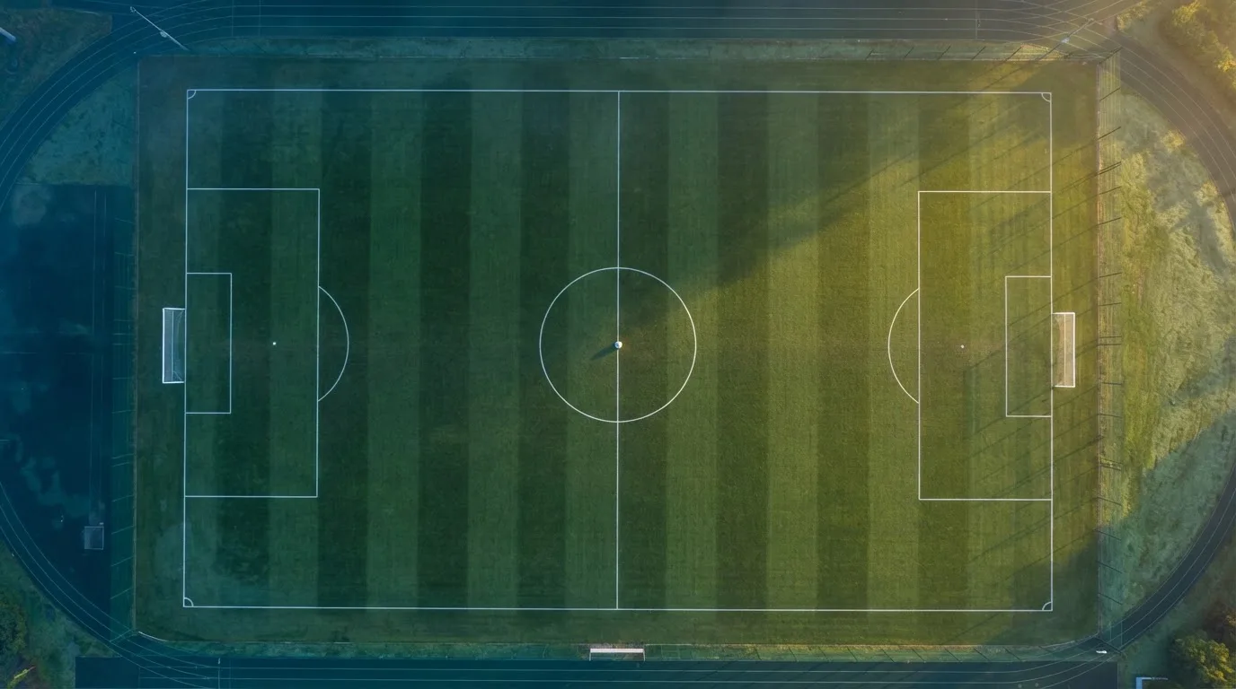 Ein Fussballplatz von oben gesehen, die Linien bilden ein helles Muster auf dem Rasen, Drohnenperspektive in der Morgendämmerung.