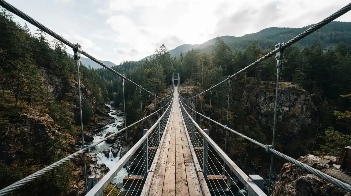 Eine Hängebrücke spannt sich über eine tiefe Schlucht, unten rauscht ein Fluss zwischen bewaldeten Felswänden.