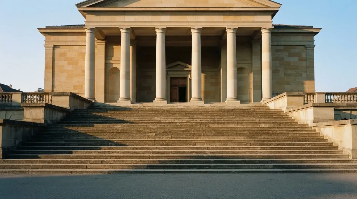 Eine breite Steintreppe führt zu einem Gebäude mit Säulen, die Morgensonne scheint, niemand ist zu sehen.